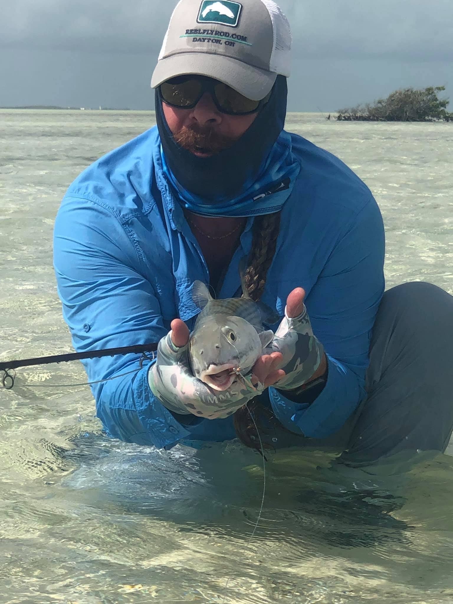 Josh showing a newly caught bonefish while kneeling on a sand flat