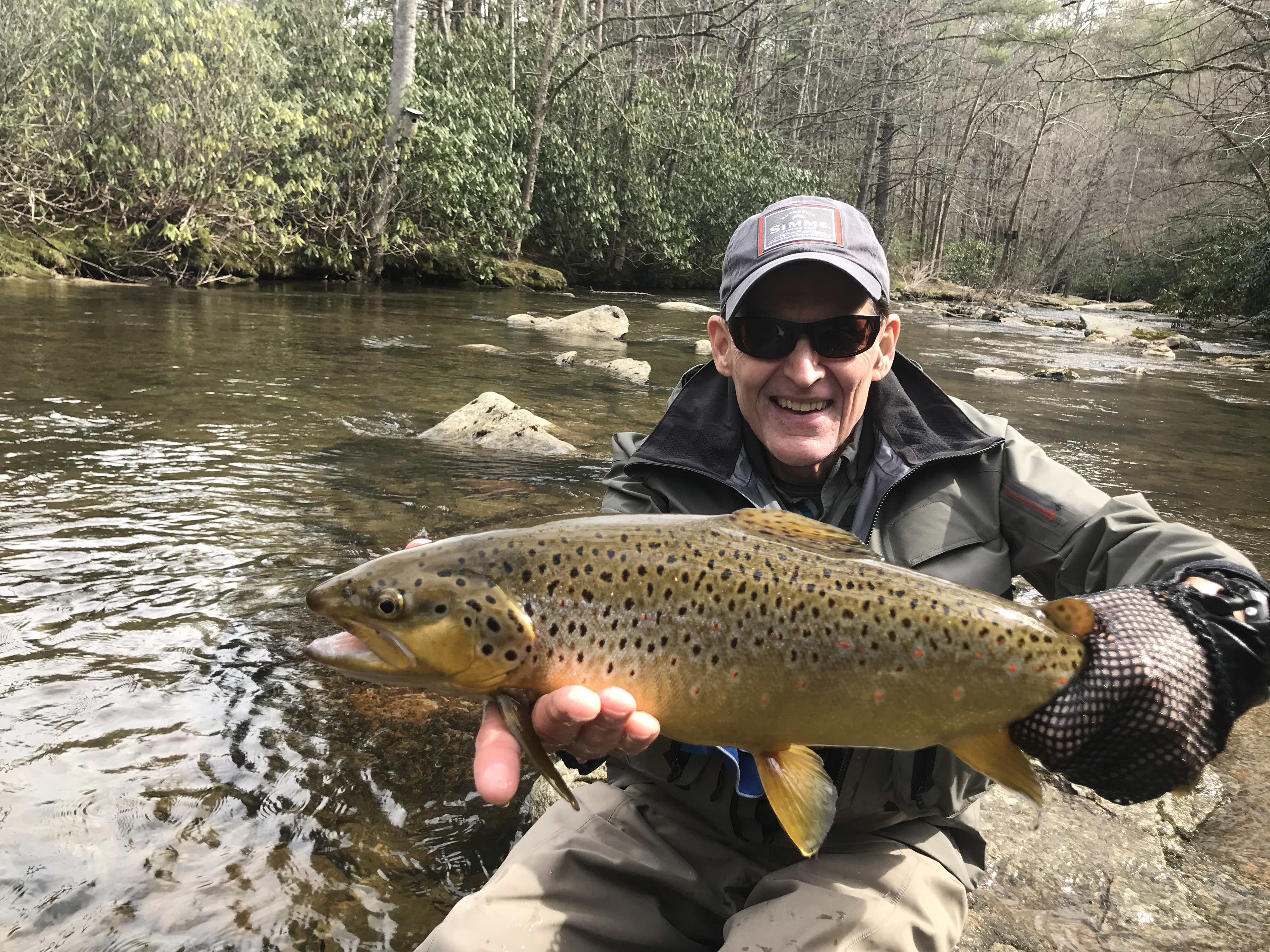 Ed kneeling by a river with a big Brown Trout