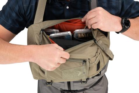 Angler searching through the Simms Tributary Sling pack filled with multiple fly boxes